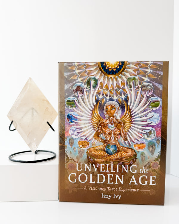 Book titled 'Unveiling the Golden Age' by Izzy Ivy on a white surface with a Golden Healer Crystal.