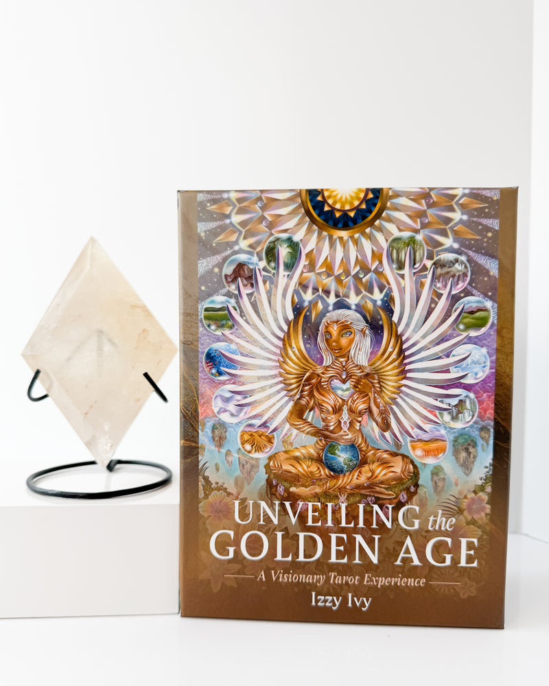 Book titled 'Unveiling the Golden Age' by Izzy Ivy on a white surface with a Golden Healer Crystal.