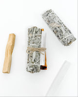 Two bundles of sage wrapped in twine with wooden tools on a white background