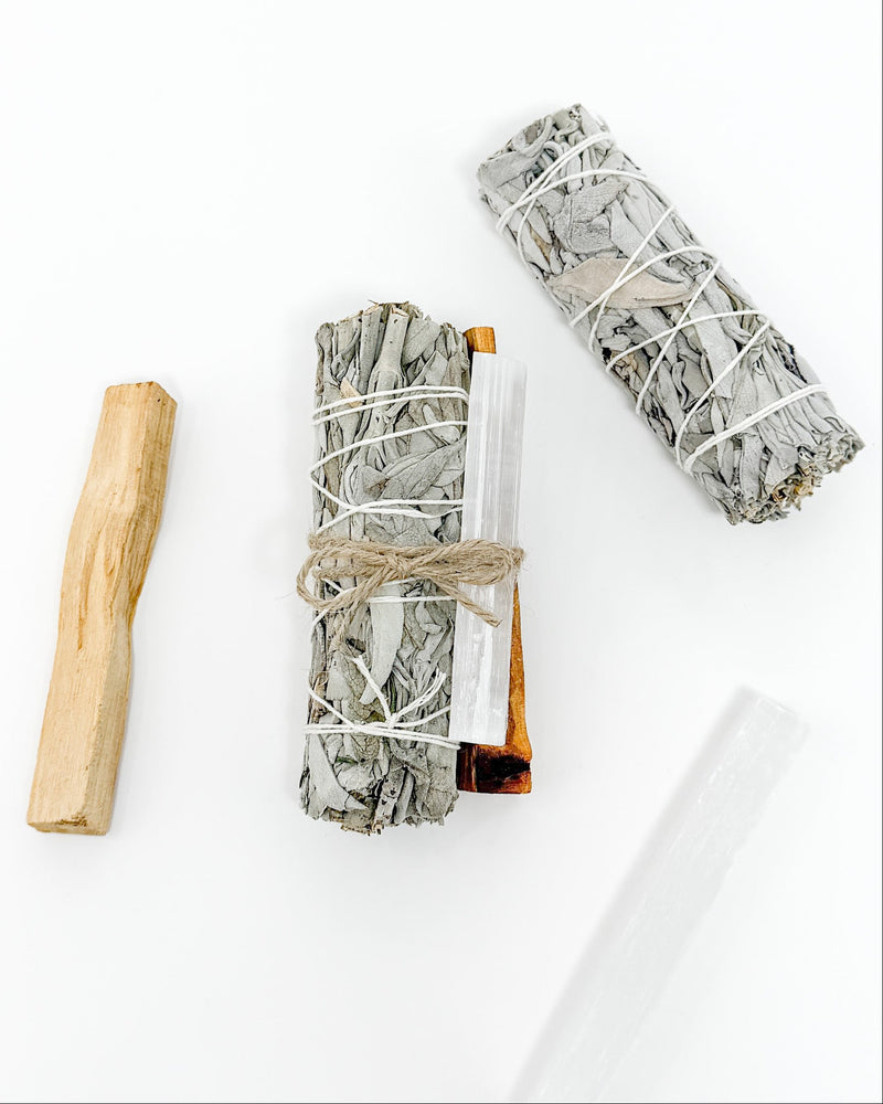 Two bundles of sage wrapped in twine with wooden tools on a white background