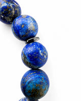 A close-up of a beaded strand featuring large, polished round lapis lazulii beads with natural gold and brown matrix inclusions, separated by small dark metal spacers, set against a plain white background.