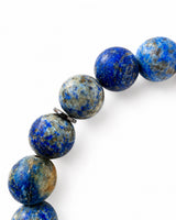 A close-up of a Lapis Lazuli beaded strand featuring polished blue and gray stone beads with metallic gold flecks, separated by small dark spacers, set against a plain white background.